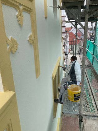 Malermeister beim streichen der Fassade auf dem Gerüst 